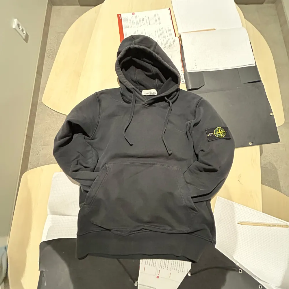 Säljer en snygg svart hoodie från Stone Island i bra skick. Den har en klassisk design med känguruficka och justerbar huva. Perfekt för både vardag och chill. Märkesloggan sitter på ärmen för en stilren look. Passar perfekt till jeans eller joggers! Har ett litet hål i armen men inget som syns eller märks. Pris ej hugget i sten!! Kom privat för mer info🙂. Tröjor & Koftor.