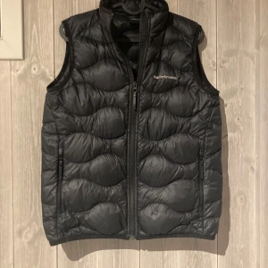 Peak performance väst svart - Säljer en svart dunväst från Peak Performance i mycket bra skick. Västen har en dragkedja framtill och är perfekt för höst och vinter. Den är quiltad för extra värme och stil. Passar både till vardags och utomhusaktiviteter.