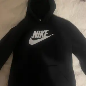 Säljer en svart hoodie från Nike i mycket bra skick. Den har en stor vit Nike-logga på framsidan och en klassisk känguruficka. Perfekt för höst och vinter, och den är superbekväm att ha på sig. Passar både till vardags och träning.