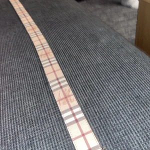 Burrberry - Säljer ett stilrent svart bälte med rutigt mönster. Perfekt för att ge en elegant touch till din outfit. Bältet har en snygg spänne och är i mycket bra skick. Passar både till vardags och fest.