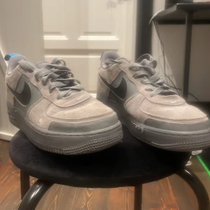 Grå Nike Air Force sneakers - Säljer ett par grå Nike Air Force sneakers i bra skick. De har en snygg kombination av ljusgrått och mörkgrått. Ursprungs pris är 1150kr. Skorna har en cool blå detalj på hälen och klassisk snörning. Perfekta för vardagsbruk och streetwear-stil.