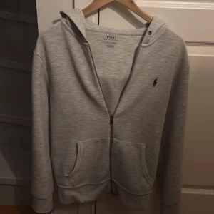 Grå hoodie från Ralph Lauren - Säljer en stilren grå hoodie från Ralph Lauren i bra skick men en liten skada på framsidan på bild nummer 4 som man knappt märker av och lite nopprig men man märker inte av det . Den har en dragkedja framtill och två praktiska fickor. Pris kan förhandlas 🧥
