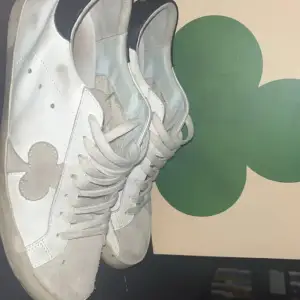 Säljer ett par vita sneakers från The Gallerist i bra skick. Skorna har svarta detaljer på hälen och ett unikt mönster på sidan. De är perfekta för vardagsbruk och har en klassisk snörning. Lite smutsiga men kan enkelt rengöras för att se fräscha ut igen. Byten är alltid intressant! 