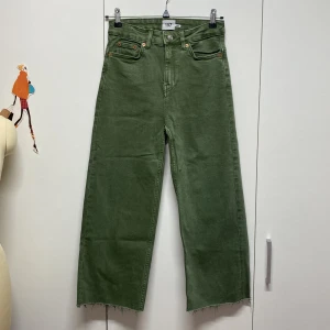 Gröna jeansbyxor - Säljer ett par gröna jeansbyxor i storlek 157. De har en högmidjad passform och är i ett loose och avslappnat snitt. Byxorna har klassiska fem fickor och en knappgylf. Perfekta för en casual look! Byxorna har ett litet hål upptill vid hällan, vilket uppstod när jag drog i dem en gång när jag tog på mig dem. Jag har även klippt av dem längst ner för att korta dem. I övrigt är byxorna som nya, då jag bara har använt dem två gånger.