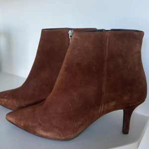 Bruna mocka stövletter med klack - Snygga bruna stövletter i mocka med spetsig tå och smal klack. Från Marian, gjorda i Spanien. Strlk 39, normal i storlek. Helt oanvända, köptes för 2899 kr.