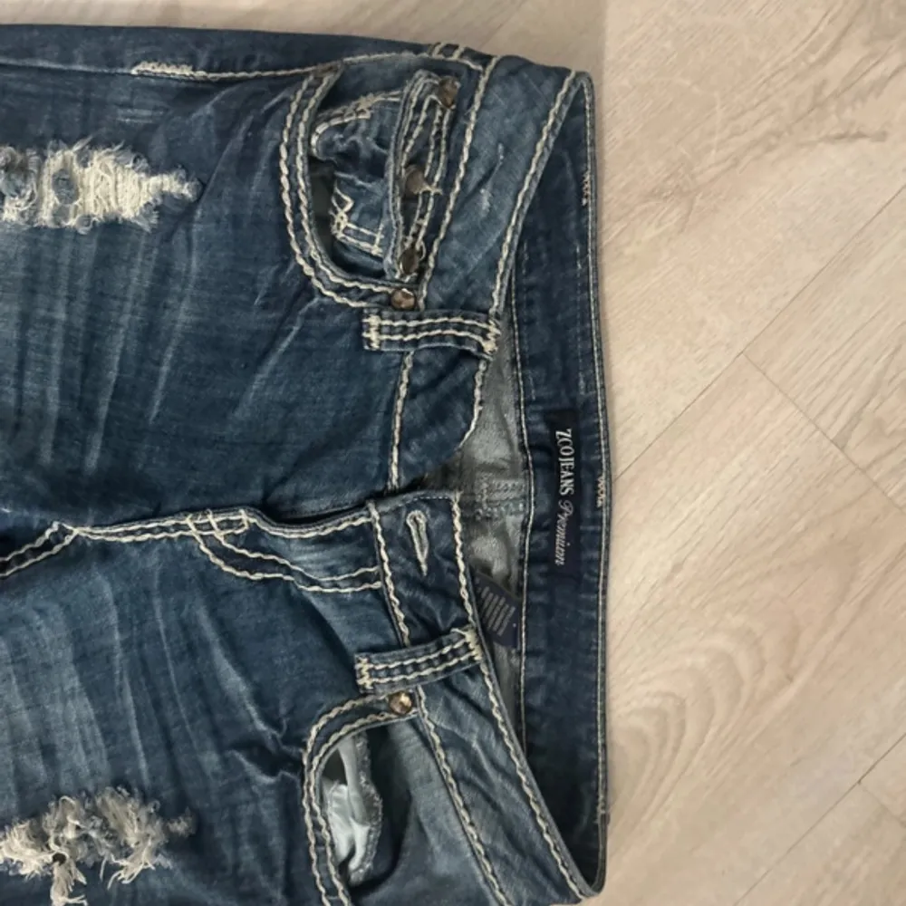 Säljer ett par snygga blå jeans från Zoe's Jeans med coola slitningar på låren. De har en klassisk femficksdesign och kontrastsömmar som ger en extra touch. . Jeans & Byxor.