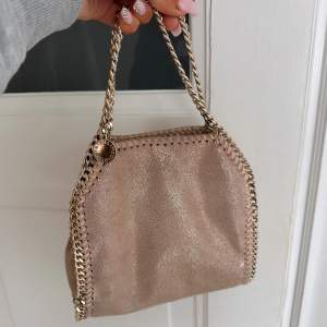 Snygg beige/rosa från Stella McCartney i mycket bra skick. Väskan har en glittrig yta och kedjedetaljer i guld. Modellen falabella. Kommer inte sälja under 5000 så ni vet då den är i väldigt fint skick! 