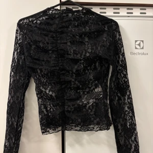 Svart spetsblus - Snygg svart spetsblus i nytt skick. Perfekt för festliga tillfällen med sitt eleganta spetsmönster. Blusen har långa ärmar och en tight passform som ger en stilren look. Nypris 329kr 