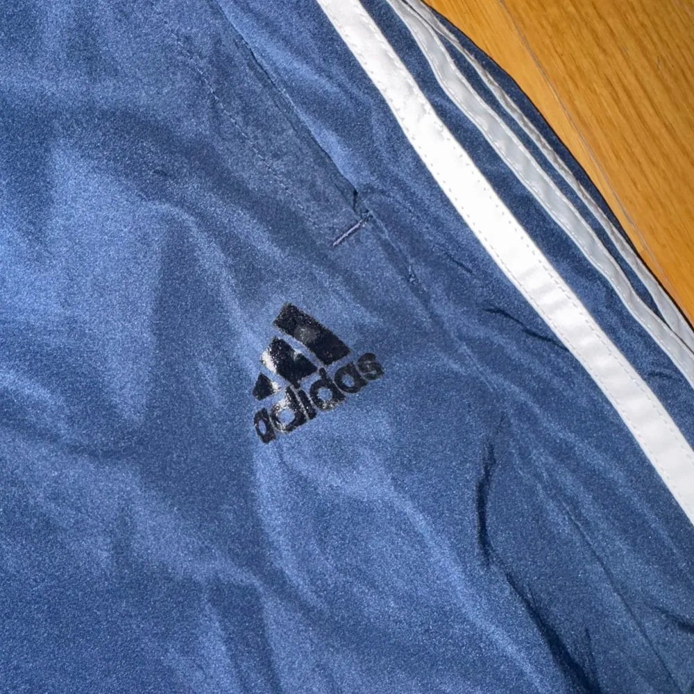 Säljer ett par mörkblå träningsbyxor från Adidas i bra skick. De har de klassiska vita ränderna längs sidorna och en elastisk midja för extra komfort. Perfekta för träning eller en avslappnad dag. 🏃‍♀️. Farkut & Housut.
