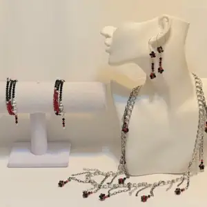 Snyggt smyckeset med halsband, armband och örhängen. Setet har silverfärgade kedjor med svarta och röda pärlor som detaljer. Perfekt för att ge en edgy touch till din outfit. Passar både till vardags och festliga tillfällen. Ett par örhängen och ett par armband plus en halsband handgjorda mycket mycket fint nytt oanvänd 