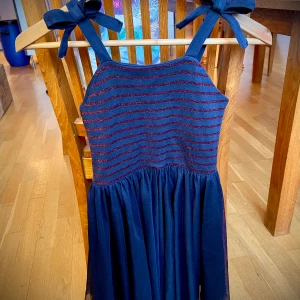 Julklänning från Petit Bateau 8 år - Söt klänning från Petit Bateau i mörkblått med glittriga röda ränder. Den har axelband med knytning och en dragkedja i ryggen. Perfekt för både vardag och festliga tillfällen. Klänningen är i mycket bra skick och gjord av mjukt material för bekväm passform. Strumpbyxor från Polarn o Pyret i storlek 122/128 i mycket bra skick ingår!