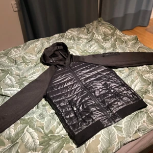 Svart jacka från Jack & Jones - Säljer en snygg svart jacka från Jack & Jones. Den har en quiltad design på framsidan och baksidan med svarta ärmar och huva. Perfekt för höst och vår! Jackan har dragkedja och är i mycket bra skick. Passar både till vardags och lite mer avslappnade tillfällen. Skriv vid minsta fundering. Pris går att diskuteras😊