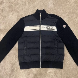 Mörkblå Moncler Cardigan - Säljer en snygg mörkblå Moncler Cardigan i mycket bra skick. Den har en quiltad framsida med dragkedja och Moncler-logga på bröstet. Ärmarna och baksidan är stickade vilket ger en cool kontrast. Perfekt för dig som vill ha något lyxigare än dem andra uttjatade cardigansen. Perfekt för nuvarande och kommande årstider. Köpt på Mytheresa för €860 och box samt alla tags tillkommer. Finns små defekter så skriv PM för detaljer. Fraktar samma dag som beställning på köparens bekostnad. 