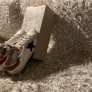Golden goose skor  - Säljer ett par Golden Goose sneakers i vitt med en svart stjärna på sidan och bruna detaljer vid hälen. Skorna är i väldigt bra skick med original box och etikett kvar. Storlek 41 men passar även mig som normal vis har 42. Mvh 101 store🤘🏼🙌🏼