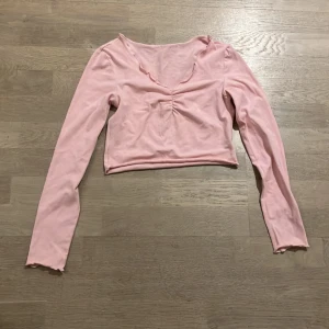 Rosa långärmad croppad topp - Säljer en söt rosa långärmad topp i croppad stil. Den har en fin rynkdetalj framtill och en mjuk, bekväm passform. Perfekt för vår och sommar!