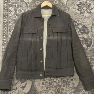 Grå japansk designer jeansjacka PPFM  - Säljer en snygg grå jeansjacka från PPFM i storlek S. Jackan har en klassisk design med knappar framtill och två bröstfickor med lock. 