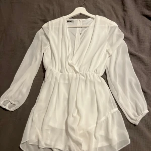 Vit omlottklänning från DM RETRO  - Säljer en superfin vit omlottklänning från DM RETRO. Den har långa ärmar och en v-ringad design som ger en elegant look. Perfekt för vår och sommar! Klänningen är i mycket bra skick och passar till både vardag och fest. Klänningen har även inbyggda shorts för en ännu mer bekväm känsla. 🤍