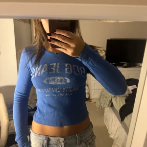 Blå långärmad topp från BDG Jeans - Säljer en snygg blå långärmad topp från BDG Jeans. Den är croppad och har ett tryck framtill. Perfekt för en casual look eller att matcha med dina favoritjeans. Toppen är i bra skick och redo för nya äventyr!