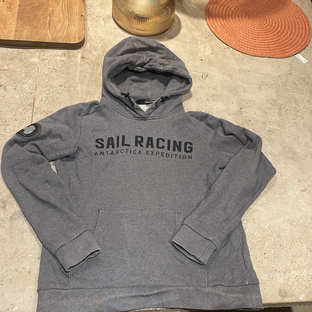 Säljer en tvärfet grå hoodie från Sail Racing med texten 'Antarctica Expedition' tryckt på framsidan. Perfekt till vardagen, och riktigt snygga detaljer vid luvan ✨🌊Storlek 170 så för liten på mig. Har en liten liten defekt vid sidan på knappt 1 cm, så väldigt lätt att laga . Hoodies.