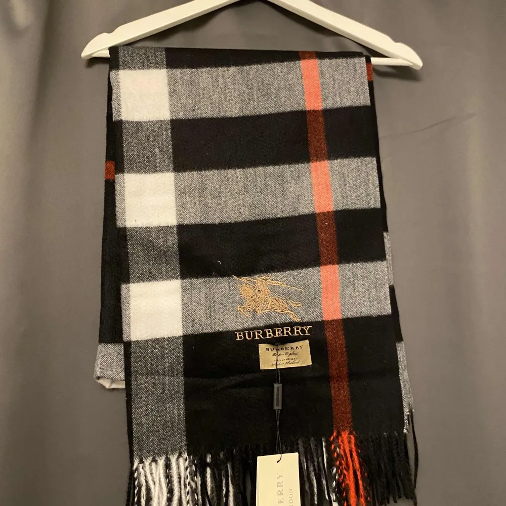 Säljer en superfin rutig halsduk från Burberry i klassiska färger som svart, grå och vit med en touch av röd. Den är i nytt skick och kommer med originalförpackning. Perfekt för att hålla sig varm och stilren under höst och vinter. 🧣✨. Övrigt.