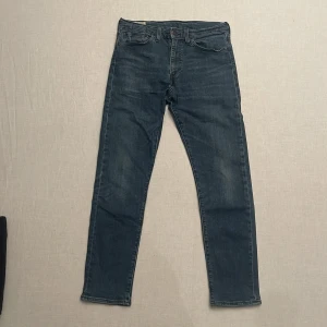 Levi's Premium Jeans - Säljer ett par snygga Levi's Premium jeans i blå denim. De har en klassisk femficksdesign och en bekväm passform. Perfekta för både vardag och fest! Bra skick förutom taggen som blivit sliten från tvätten (bild 4). Sitter slim/skinny och är strl. W32 L32 