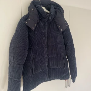 Vinterjacka Save the Duck - Säljer en snygg svart manchesterjacka från Save the Duck. Jackan är quiltad och har en avtagbar huva med knappar. Den är i mycket bra skick och perfekt för höst och vinter. Dragkedja framtill och två fickor med dragkedja. Superbekväm och stilren!  Jackan är i storlek L och har enbart används en säsong så skicket är helt perfekt. Jag köpte den förra året för 5 000kr. Sökord: Vinterjacka Jacka Manchesterjacka Save the duck Maja