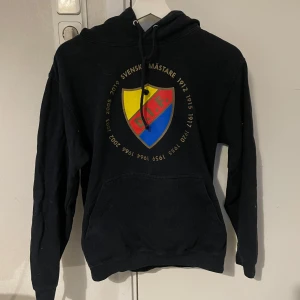 Svart hoodie med Djurgården-tryck - Intressekoll på denna svarta hoodie med Djurgården-tryck på bröstet. Perfekt för att visa ditt stöd för laget! Den har en klassisk känguruficka och justerbar huva. Passar bra till både vardag och matchdagar. Skön och bekväm att ha på sig hela dagen.