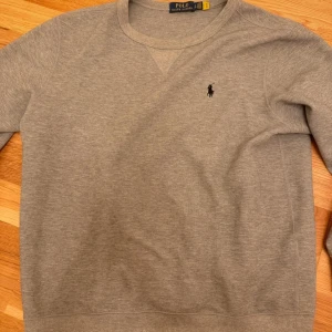  Ralph Laurent tröja  - Säljer en stilren grå tröja från Polo Ralph Lauren i storlek L. Tröjan har en klassisk design med rund hals och det ikoniska logotypbroderiet på bröstet. Perfekt för både vardag och avslappnade tillfällen. Skön och mjuk i materialet, ett måste i garderoben! Ej autentisk. Kan passa dig med storlek M