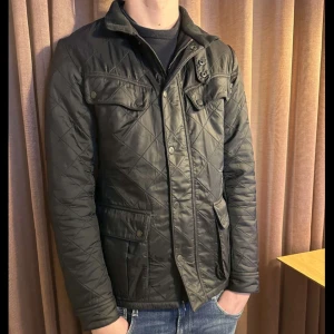 Svart quiltad jacka från Barbour - Vi säljer en snygg svart quiltad jacka i mycket bra skick. Den har en klassisk stil med dragkedja och knappar framtill, samt praktiska fickor. Perfekt för höst och vår, och passar både till vardags och lite finare tillfällen. Jackan är långärmad och har en normal passform. Skick- 8/10 med en slitning på ena ärmen, knappt så att man lägger märke till det. Nypris 3499. Tveka inte på att höra av dig vid frågor eller intresse!💫