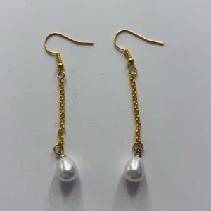 Guldörhängen med pärlor - Snygga guldörhängen med en elegant kedja och vita pärlor som hänger längst ner. Perfekta för att ge en touch av glamour till vilken outfit som helst. De är lätta och bekväma att bära hela dagen. Passar både till vardag och fest!