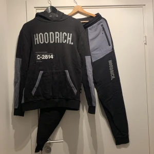 Svart och grå hoodie och byxa från Hoodrich - Säljer en snygg svart hoodie och byxor från Hoodrich med grå detaljer och text. Den har en stor ficka fram och är perfekt för en casual look. Passar bra till höst och vinter. Stor logga på bröstet och cool design.