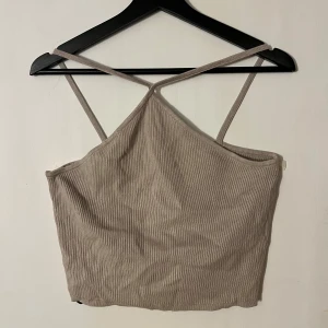 Beige ribbad linnetopp - Säljer en superfin beige ribbad linnetopp i nytt skick. Den är ärmlös med smala axelband som korsas vid bröstet/halsen. Passar både till vardags och fest! Köpt för 149kr o aldrig använt, prislappen sitter kvar.