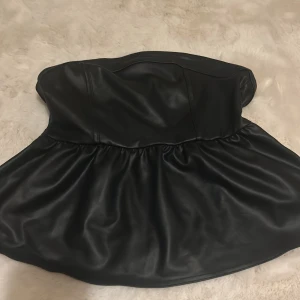 Svart tubtopp från H&M Divided - Snygg svart tubtopp i skinnimitation från H&M Divided. Toppen har en dragkedja och är jätte bekväm. Aldrig använd 