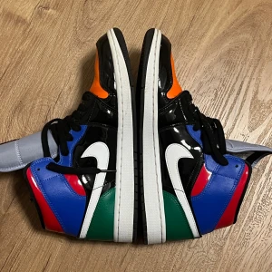 Flerfärgade Nike Air Jordans - Snygga och iögonfallande Nike Air Jordans i en mix av färger som svart, vit, blå, grön, röd och orange. Skorna har en klassisk design med snörning och den ikoniska swoosh-loggan på sidan. Perfekta för dig som vill sticka ut!