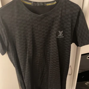 Svart t-shirt  - Snygg svart t-shirt från med diskret rutmönster och logga på bröstet. Perfekt för en stilren look.