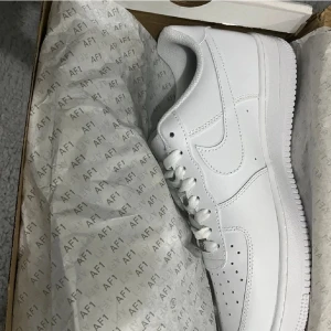 Vita Nike Air Force sneakers - Klassiska vita Nike Air Force sneakers med snörning och perforerade detaljer på tån. Dessa sneakers är tillverkade i syntetmaterial och har en ikonisk design som passar perfekt till alla tillfällen. Aldrig använda. Pris kan diskuteras lite!!!