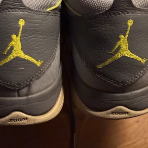 Grå Nike Air Jordans med gula detaljer - Snygga grå Nike Air Jordans med gula detaljer och snörning. Skorna har en robust sula med mönster och den ikoniska Jumpman-loggan i gult. Perfekta för dig som vill ha en stilren och sportig look.