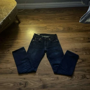 Levis 501 jeans i mörkblå denim - Klassiska Levis 501 jeans i mörkblå denim. De har en rak passform och är midwaist. Perfekta för en tidlös stil. Storlek W27 L30. Jeansen är i bra skick men några tecken på användning. Kontakta mig vid funderingar.