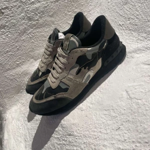 Camouflage sneakers från Valentino - Snygga sneakers från Valentino med ett coolt camouflage-mönster i grå och svarta toner. Skorna har snörning och en robust sula för extra komfort. Perfekta för en stilren och avslappnad look.