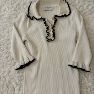 Vit blus med svarta och pärldwtaljer från ”Holly and Whyte, Lindex” - Säljer denna eleganta blusen/toppen med armar som slutar på mitten av armen.Blusen har bara används en gång , har inte a haft chansen att använda andra gånger.Ordinariepriset på denna blus var 400 kr!