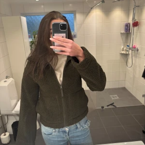Olivgrön teddyjacka - Mysig olivgrön teddyjacka med dragkedja framtill. Perfekt för kyliga dagar med sin fluffiga och varma design. Jackan har en normal passform och långa ärmar. Passar mig som är en S!