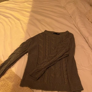 Grå stickad tröja från 157 - Säljer en mysig grå stickad tröja från 157. Tröjan har ett klassiskt flätmönster och långa ärmar. Perfekt för kyliga dagar. Passar bra till jeans eller kjol. 🧶