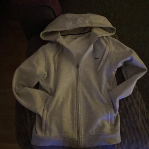 Grå hoodie från Lacoste Sport - Säljer en stilren grå hoodie från Lacoste Sport. Den har en dragkedja framtill och en klassisk huva. Perfekt för en avslappnad stil. 🐊