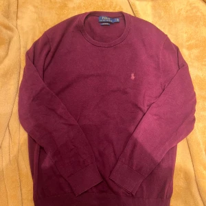 Vinröd crewneck Ralph Lauren - Säljer en stilren vinröd tröja från Polo Ralph Lauren i mjuk bomull. Tröjan har en klassisk rund hals och långa ärmar med ribbade muddar. Perfekt för en avslappnad men elegant look.