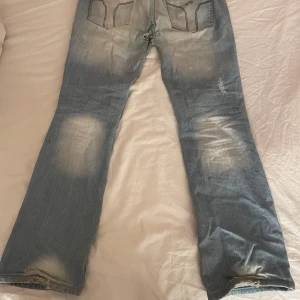 Blå jeans med slitningar - Säljer ett par blå jeans med slitningar och en ljus tvätt. De har en bootcut-stil och är lågmidjade. knappt använda och i strl 28 men har sattit skosnören på insidan så de går att spänna utan att de syns på utsidan!