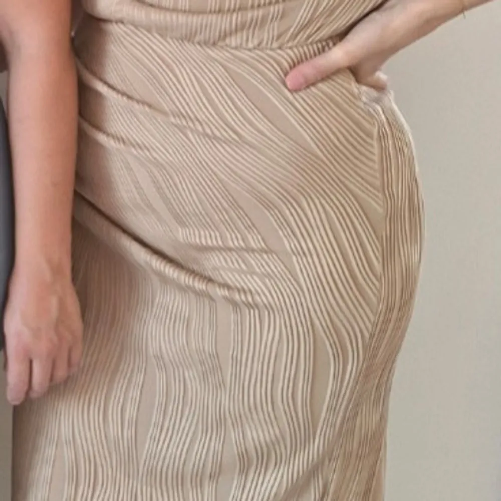 Säljer en elegant beige klänning med ett subtilt randigt mönster. Klänningen har en smickrande passform och är perfekt för en stilren look. Den är tillverkad i ett mjukt och bekvämt material.. Mekot.