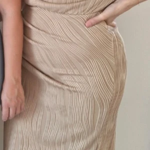 Beige omlottklänning - Säljer en elegant beige klänning med ett subtilt randigt mönster. Klänningen har en smickrande passform och är perfekt för en stilren look. Den är tillverkad i ett mjukt och bekvämt material.