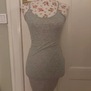 Grå ärmlös klänning - Snygg och enkel grå klänning i tight passform. Den är ärmlös med smala axelband som korsas i ryggen. Perfekt för en avslappnad stil. Storlek XS. Mycket bra skick då den nästan aldrig blivit använd. 