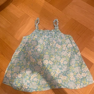 Blommig linnetopp i blått och gult - Söt blommig linnetopp i blått med vita och gula blommor. Toppen har smala axelband och en luftig passform, perfekt för varma dagar. Såå söt