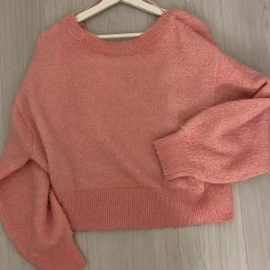 Rosa stickad tröja - Mysig rosa stickad tröja med v-ringad design och långa ärmar. Perfekt för kyligare dagar med sin mjuka och bekväma passform. Ribbstickade muddar vid ärmslut och nederkant ger en stilren look.